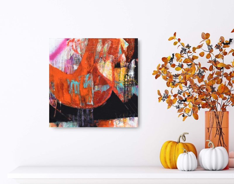 An orange, white, black, pink, and teal mixed media abstract painting, titled "Heavy is the Head" by Kathryn Gruber hangs on a white wall above a white shelf. To the right are several decorative pumpkins, the larger which is orange, the other smaller two white, all with curly stalks. Behind them is an orange glass vase with several springs of orange foilage placed in it.